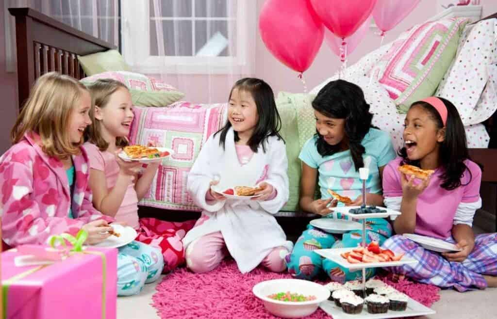 Group of girls laughing and enjoying snacks while playing Two Truths & A Lie at a fun sleepover party