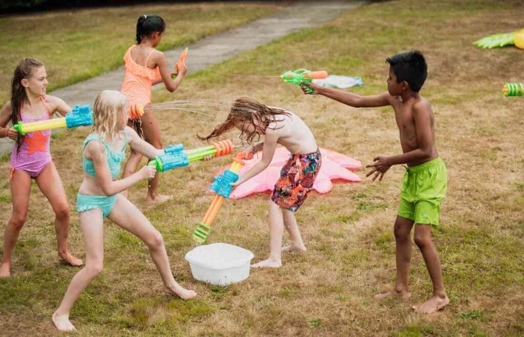 Kids having fun with water blasters in a backyard Nerf war or laser tag birthday party