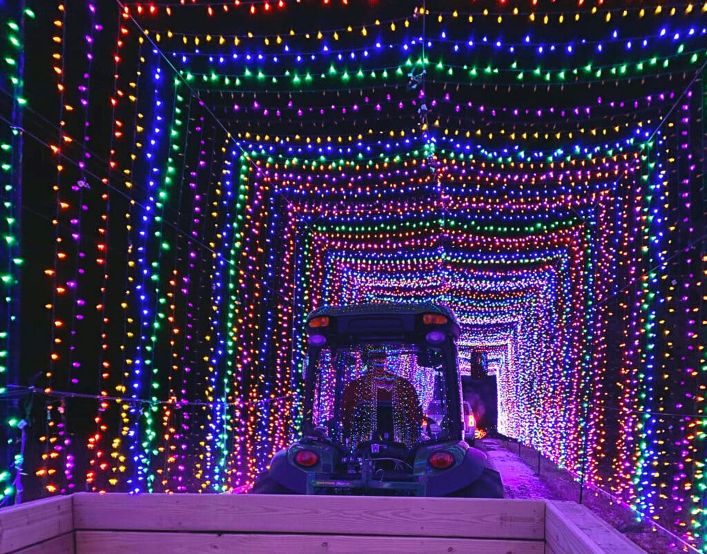 Tractor pulling a wagon ride through a tunnel of colorful holiday lights at Country Christmas in The Ingleside Hotel, Wisconsin.