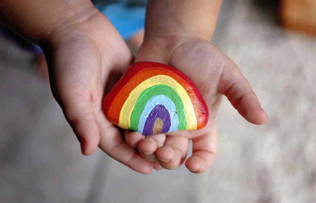 Painting rocks shape activity toddler holding rainbow rock.