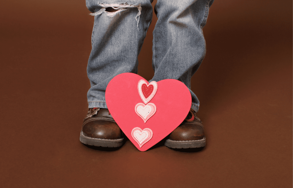 Valentine at the feet of a little boy with jeans and brown shoes.