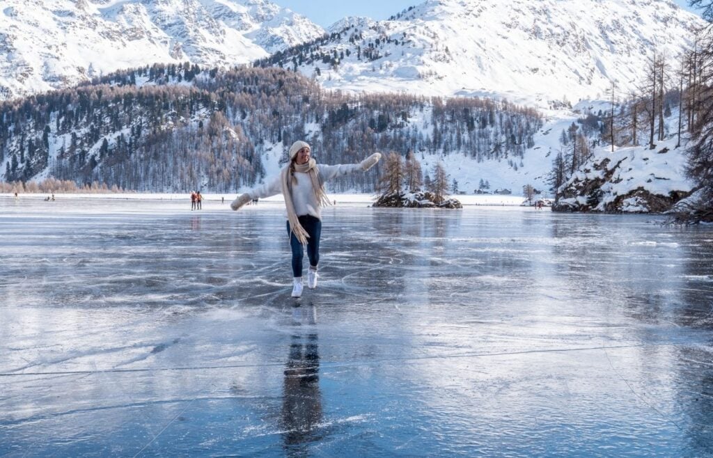 Woman ice skating on a pond with snow covered mountains in the background.