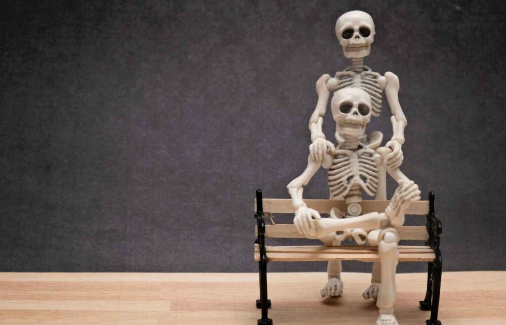 Skeleton couple, one sitting on a bench and the other with their hands on the other's shoulder.