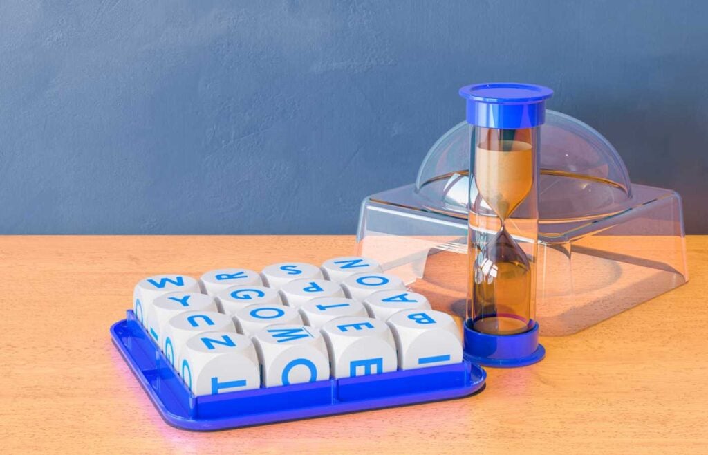 Boggle word game set on a wooden surface, featuring a grid of lettered dice and an hourglass timer