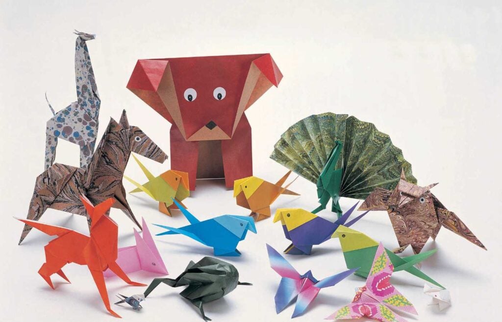 Colorful paper origami animals, including a giraffe, dog, birds, and fan, arranged together on a white surface, representing an origami competition for a fun and creative activity.