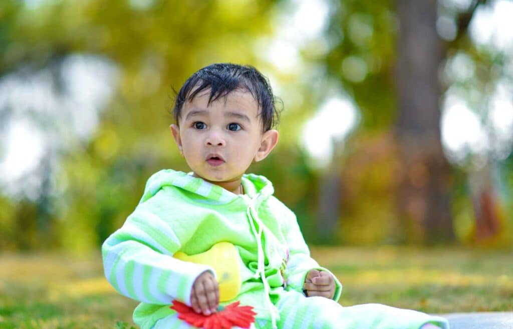 Cute baby boy in a green hoodie holding a flower, evoking growth and the purity of baby names like Pooranjit.