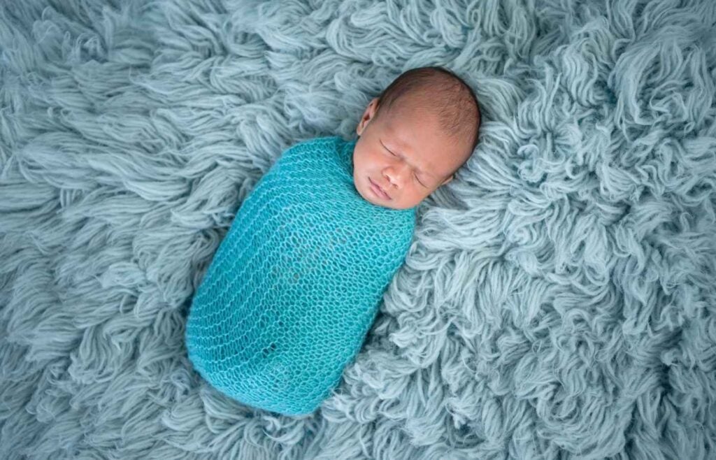 Baby boy bundled in blanket on blue rug