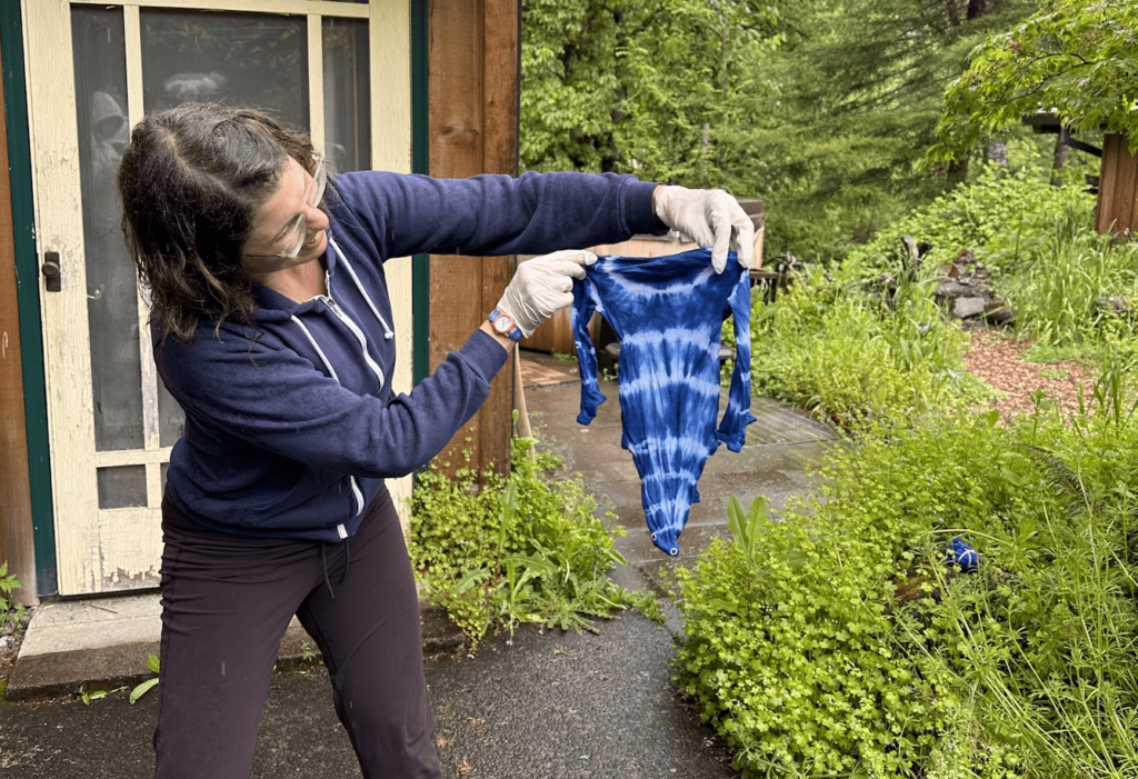 Woman in a sweatshirt holding her folded pattern indigo tie dyed baby onesie