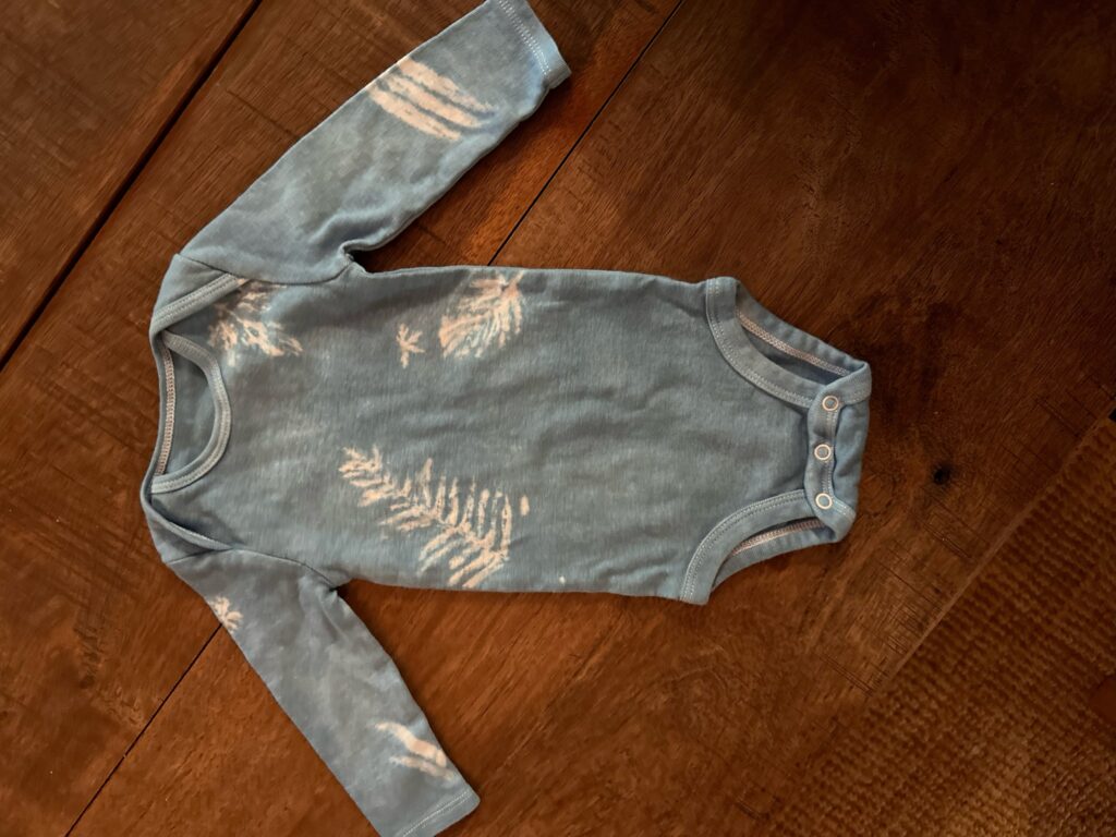 Light blue baby onesie tie dyed with indigo tie dye using a leaf pattern