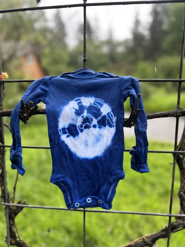 Baby onesie with indigo tie dye sunburst pattern hanging to dry outside