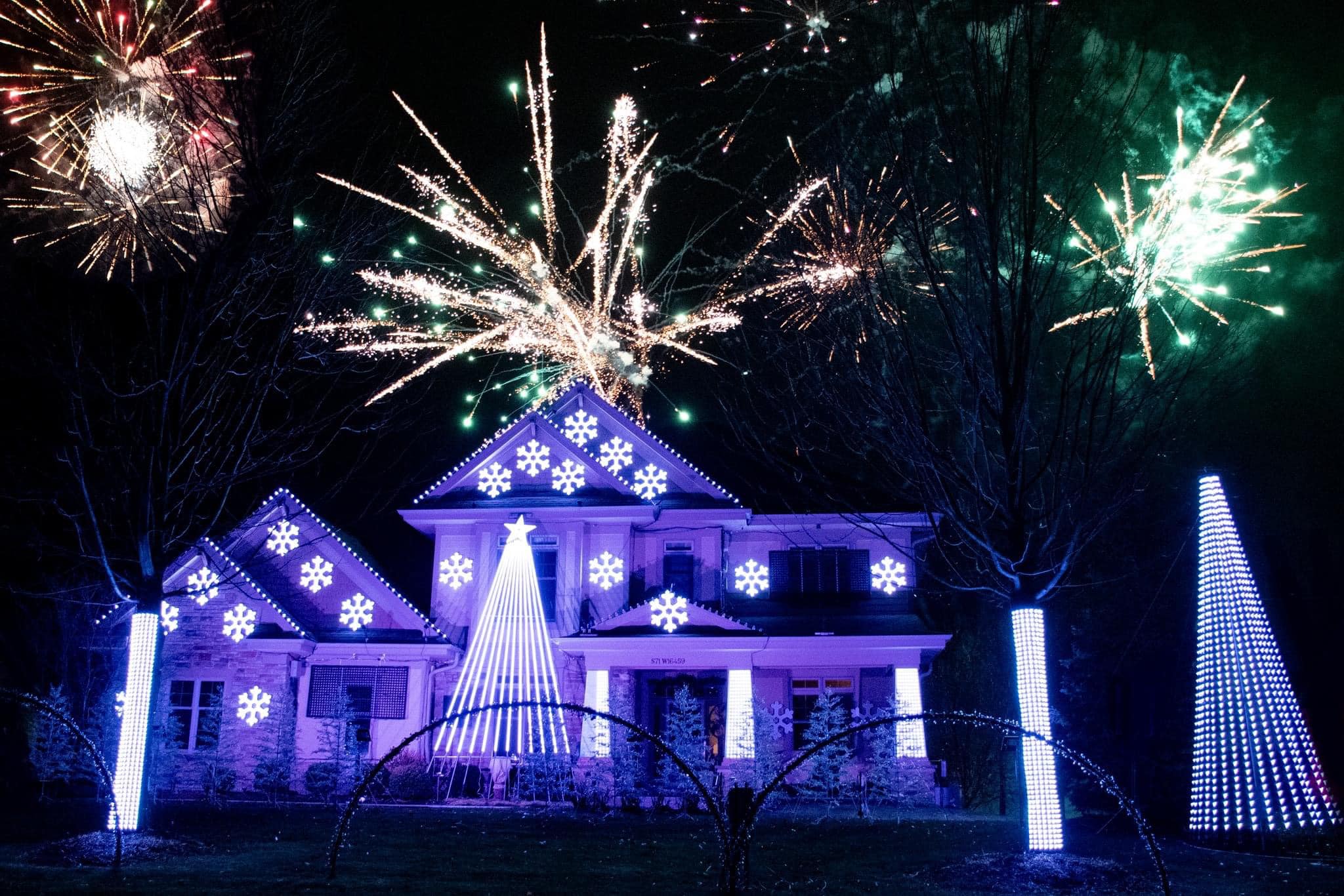 House decorated with over 35,000 LED lights synchronized to music at Lights on Glen Cove, with fireworks lighting up the sky above.