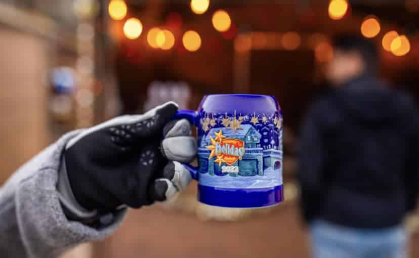 Gloved hand holding a festive holiday mug at the Wauwatosa Christkindlmarkt, with warm lights and a cozy holiday atmosphere in the background.