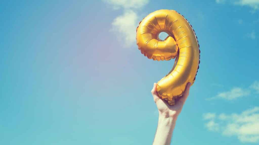 Gold number 9 balloon held up against a clear blue sky for a child's 9th birthday celebration.