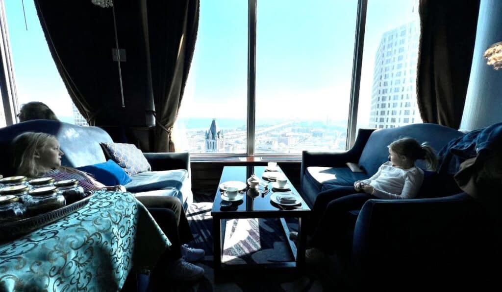 Two girls enjoying a quiet moment by a large window, overlooking the city during afternoon tea at The Pfister Hotel.