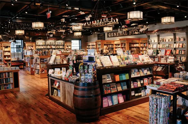 Interior of An Unlikely Story Bookstore, featuring wooden floors, chandeliers, and shelves filled with books. The cozy atmosphere is enhanced by warm lighting and inviting displays, creating a welcoming space for readers and visitors.