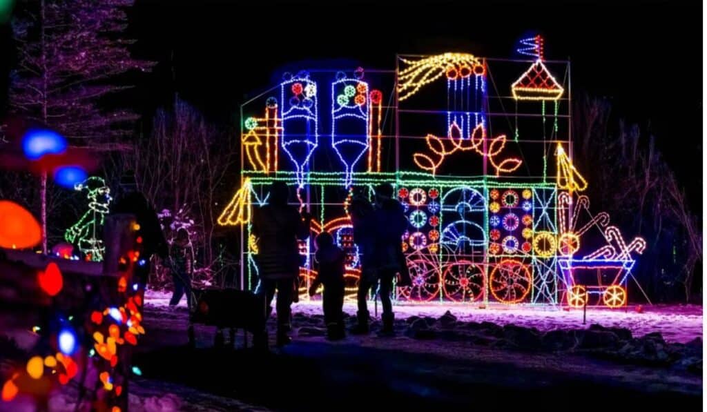  A family bundled in winter clothes stands near a large, illuminated holiday display featuring colorful lights shaped into festive scenes, capturing the magic of Country Christmas.