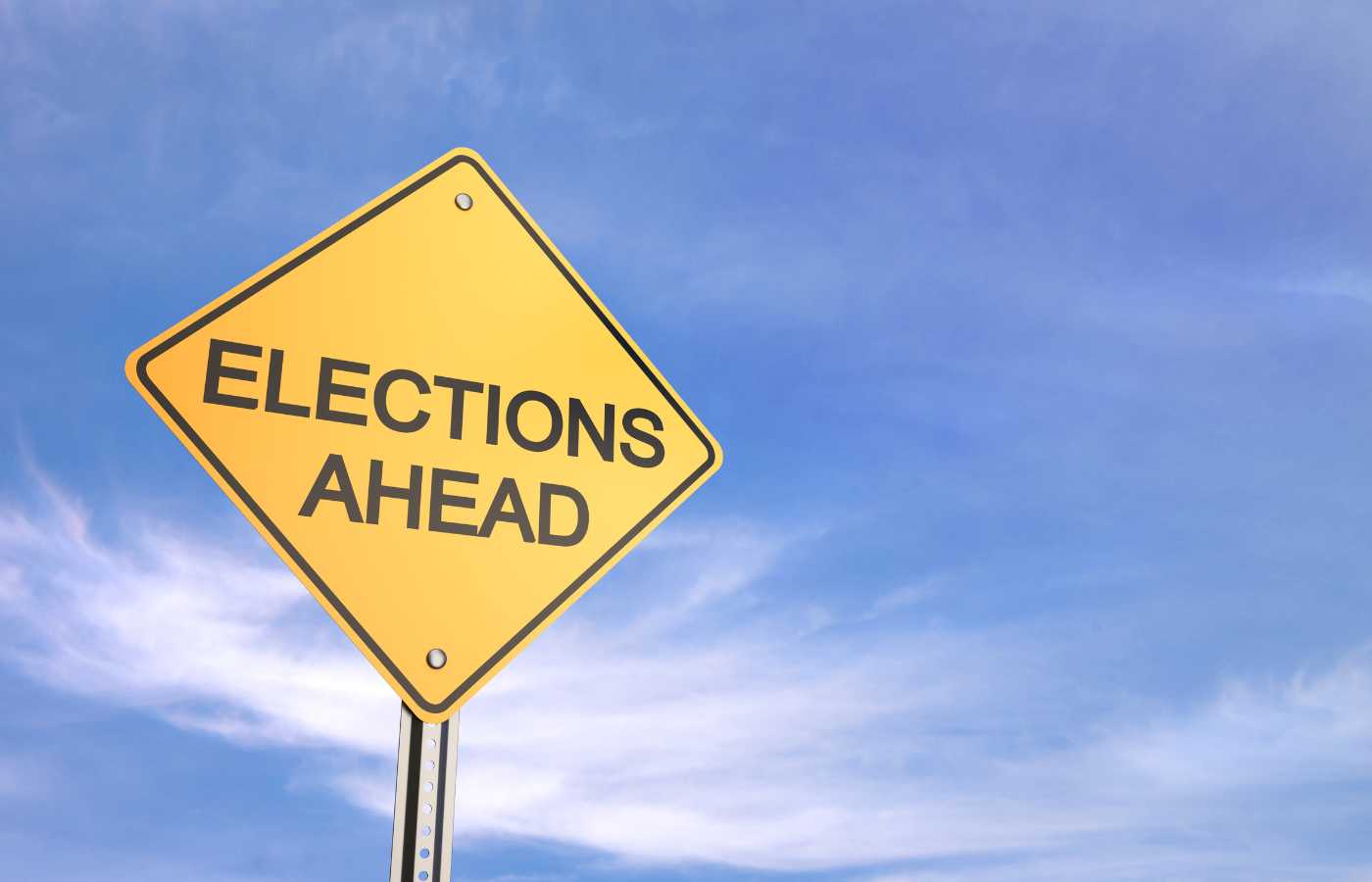 A yellow diamond shaped road sign that says "Elections Ahead' in black block letters against a blue sky with some clouds. 