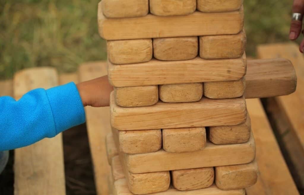 Hand pulling a wooden block from a giant Jenga tower at an outdoor birthday party