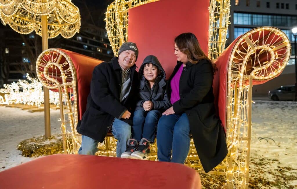 Family sitting together on a large illuminated chair at Zeidler Union Square in Milwaukee, surrounded by festive holiday lights.