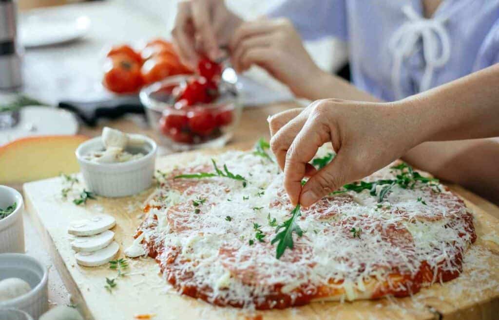 Hands adding toppings to a homemade pizza during a make-your-own pizza party for kids