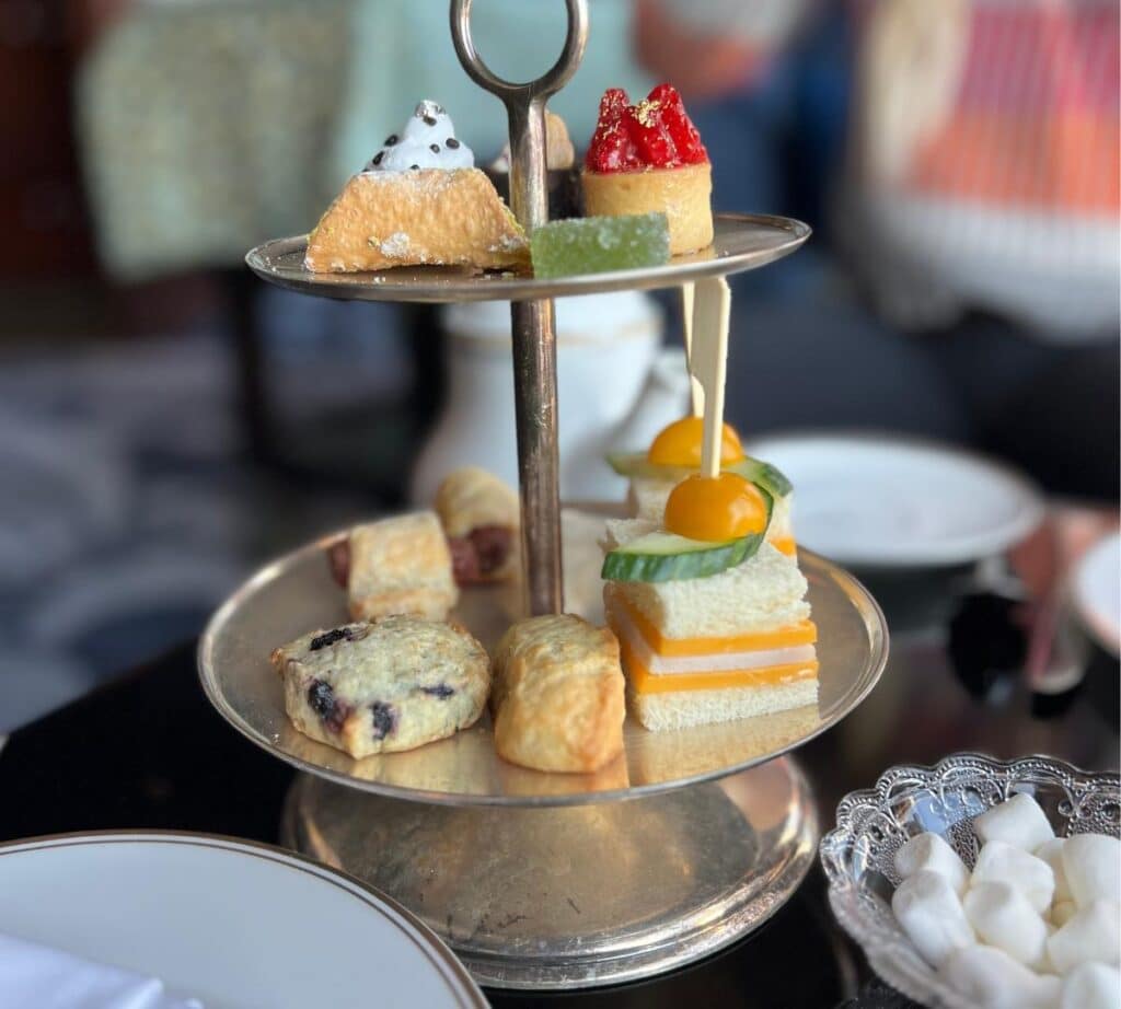 A delicious assortment of afternoon tea snacks, including savory sandwiches, sweet pastries, and scones served on a silver two-tier tray at The Pfister Hotel's afternoon tea.