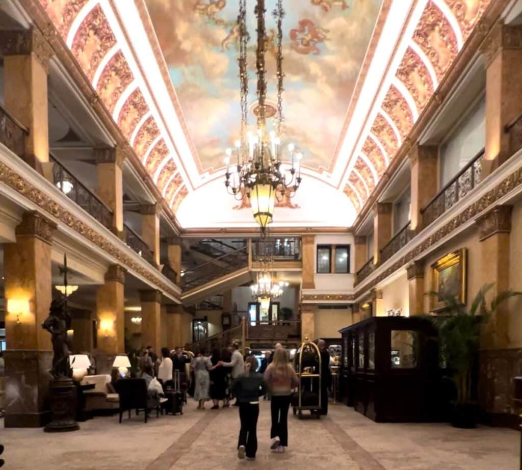 The grand lobby of The Pfister Hotel, featuring ornate chandeliers, detailed ceilings, and a luxurious atmosphere.