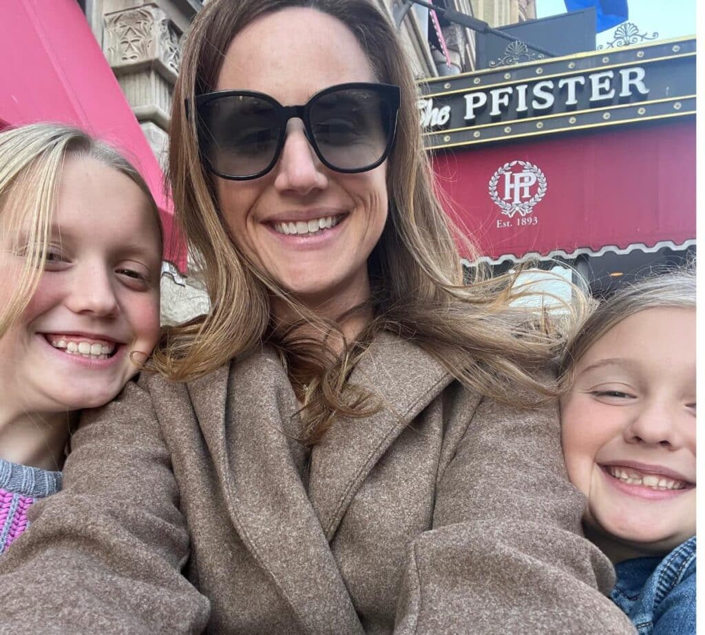 A smiling mother and two children taking a selfie outside The Pfister Hotel, ready for an afternoon tea experience.