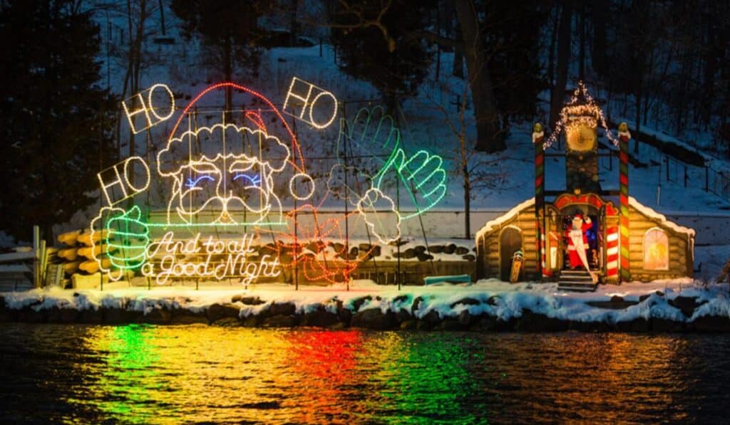 A large, historic boat on Lake Geneva covered in colorful holiday lights, reflecting in the water during the Santa Cruise.