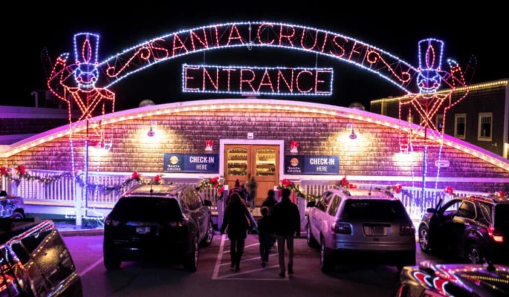 The illuminated entrance to the Lake Geneva Santa Cruise, decorated with holiday lights and festive soldiers, as families walk toward the check-in area.