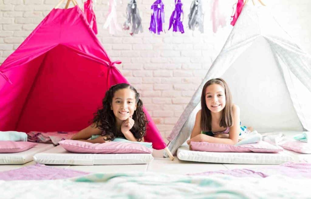 Two girls smiling and relaxing inside colorful tipi tents at a sleepover birthday party