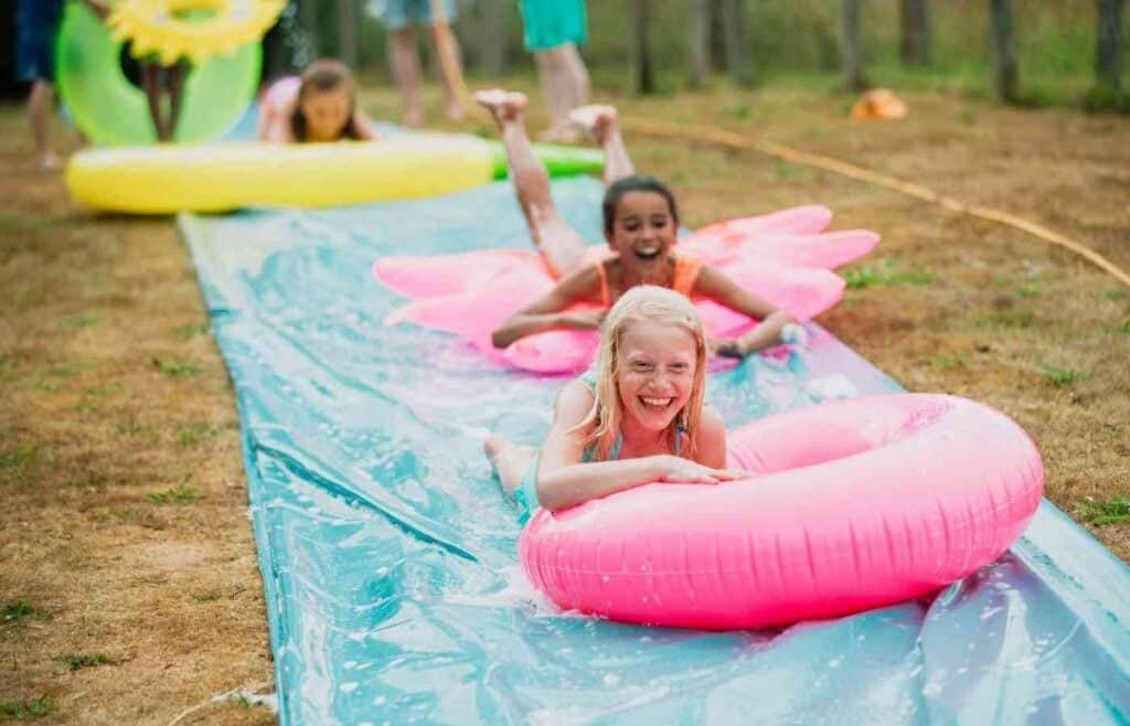 Kids having fun on a slip n' slide with colorful pool floats at a summer birthday party