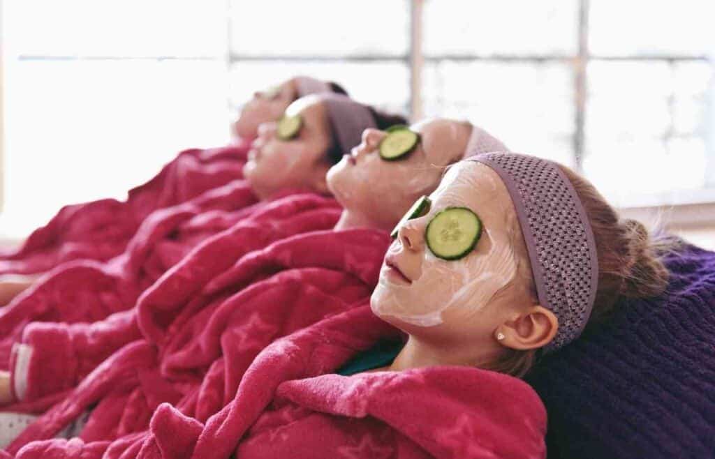 Young girls with cucumber slices and face masks relaxing at a spa-themed birthday party