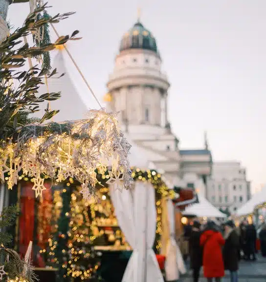 Festive holiday decorations and lit garlands at the Paoli Christkindl Market, with a scenic view of historic architecture in the background and market stalls adorned with Christmas lights.