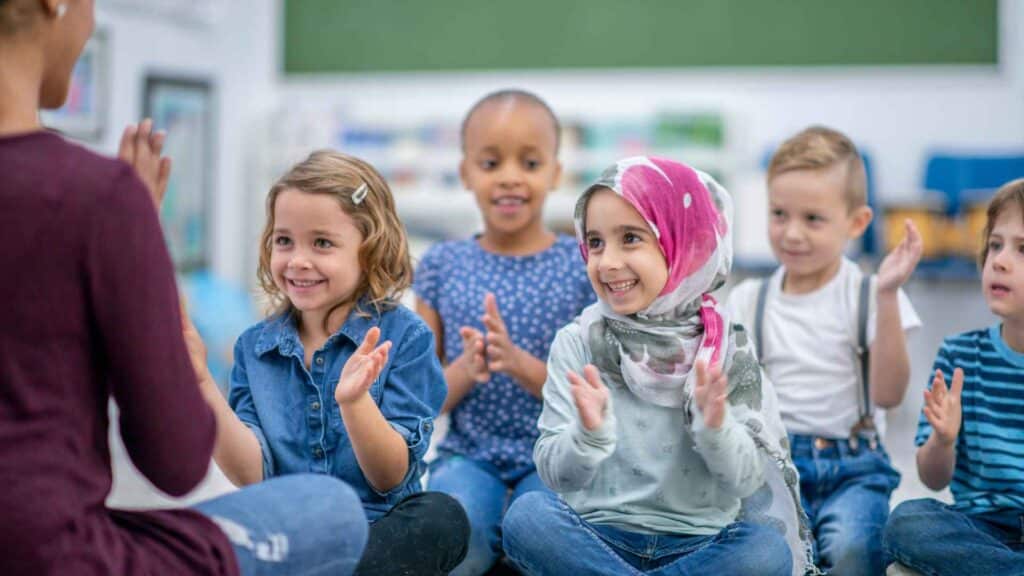 Kids clapping and looking at their teacher in a classroom